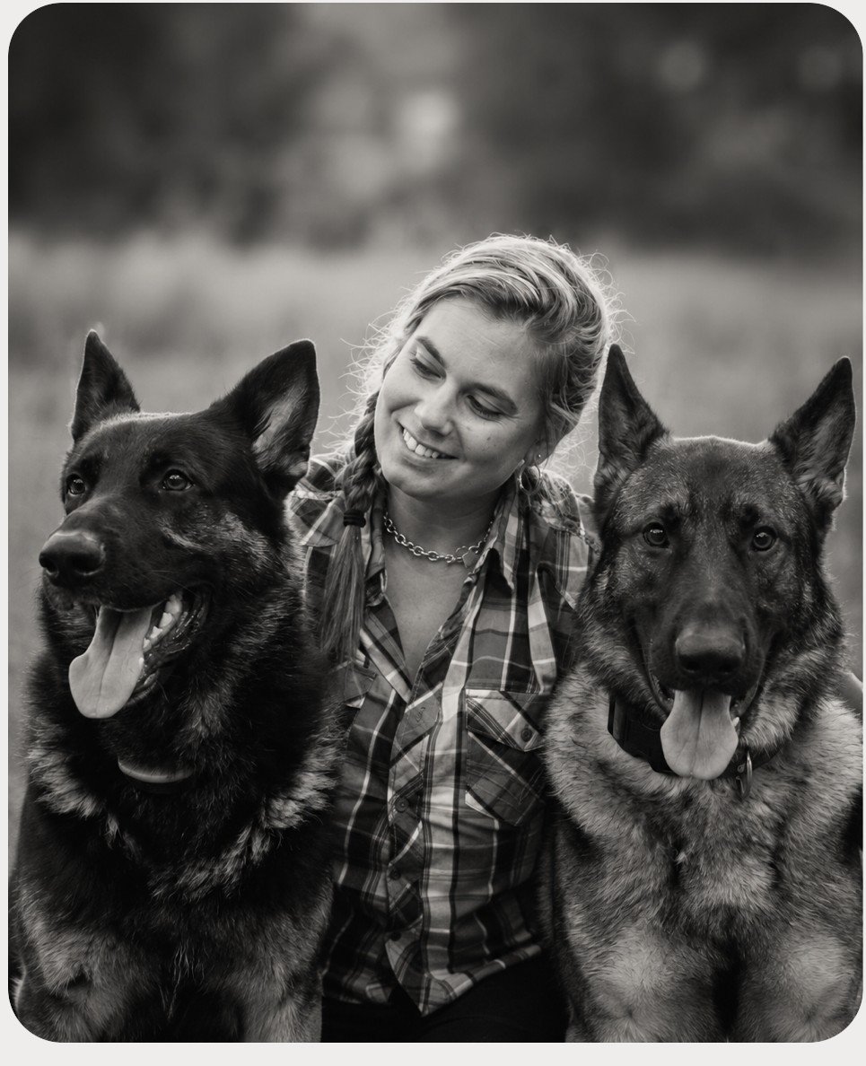 Jen Mariani kneeling between her two German Shepherds, in black and white